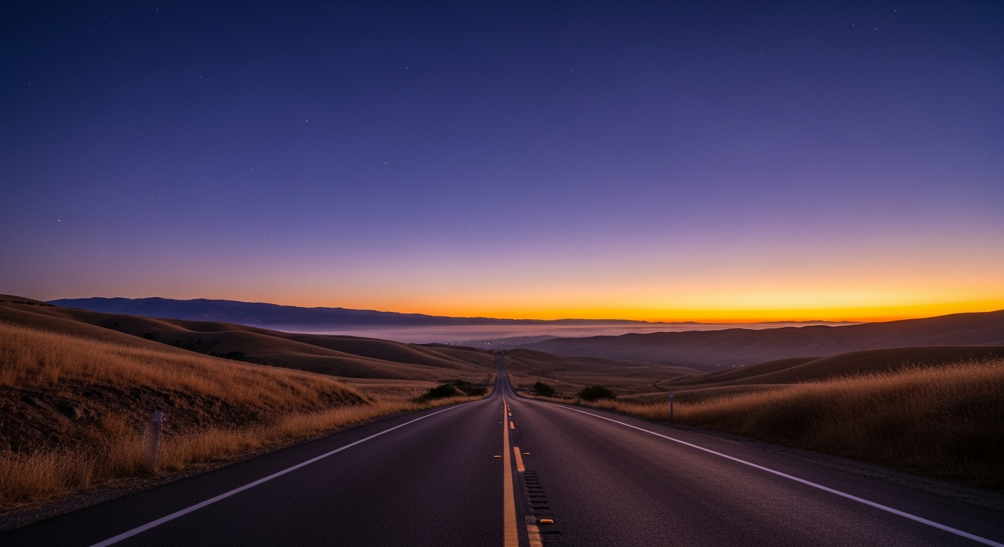 A long road winding through hills toward a dawn horizon